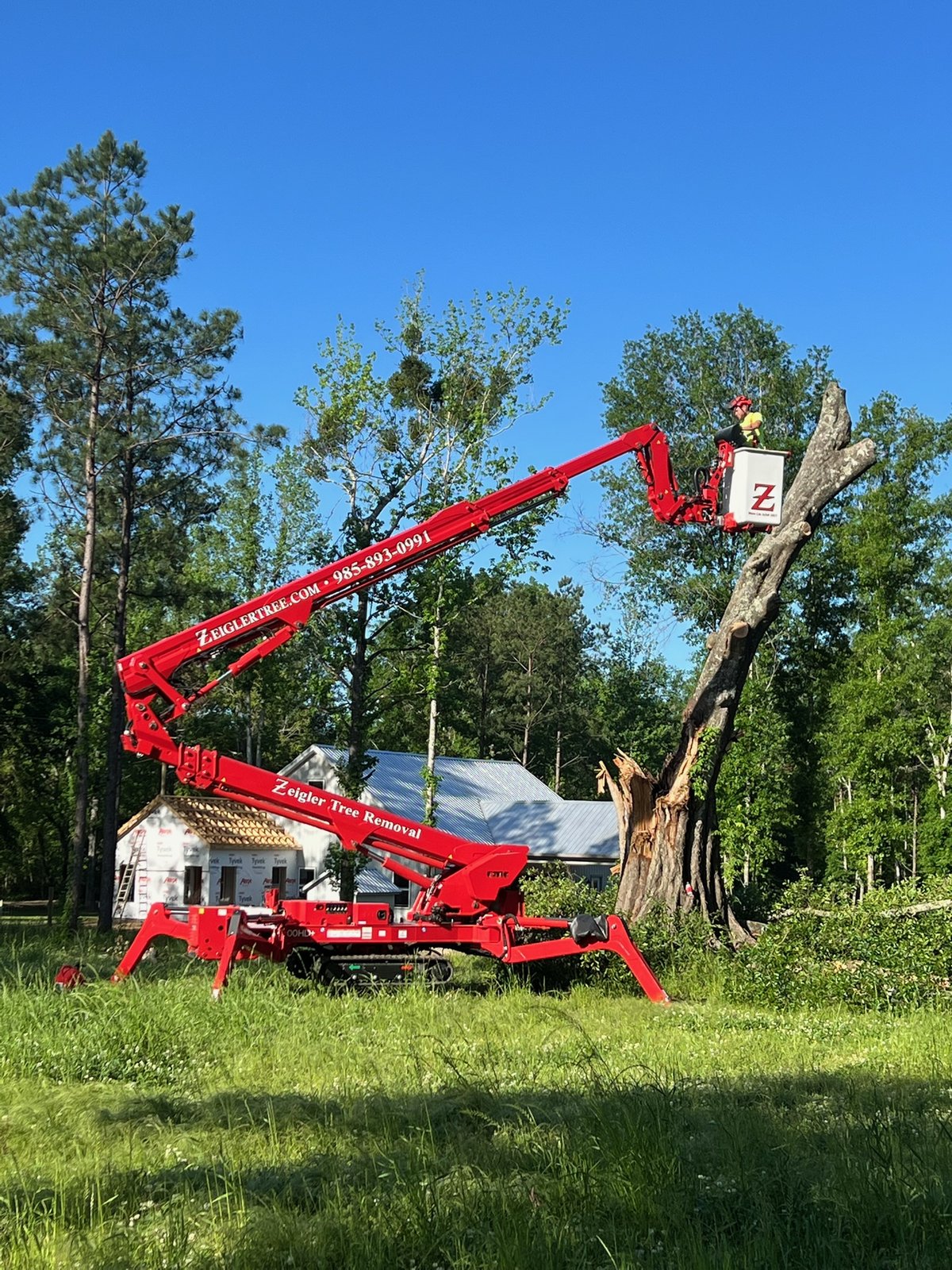Crew member in a bucket lift clearing storm-damaged limbs off a home’s roof