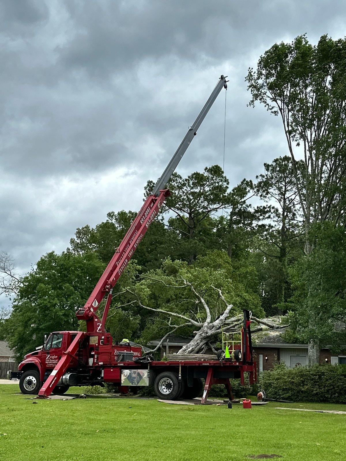 Crane truck lifting a large tree limb near a home under stormy skies